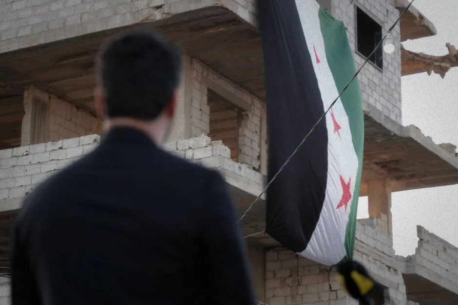 A man observes a Syrian flag draped over a war-torn building in Damascus, Syria.