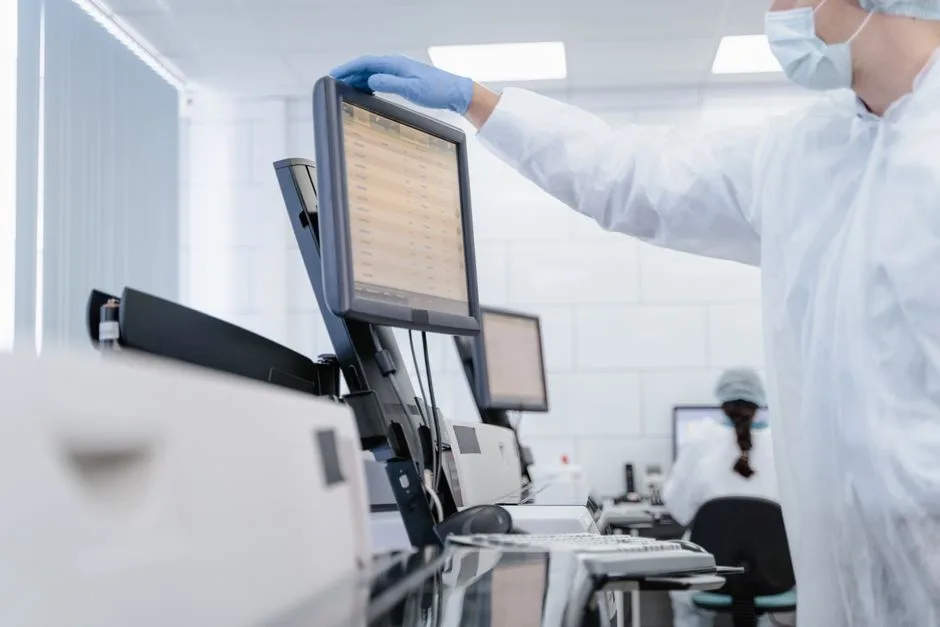 Researcher in PPE reviews data on a digital screen in a modern laboratory setting.