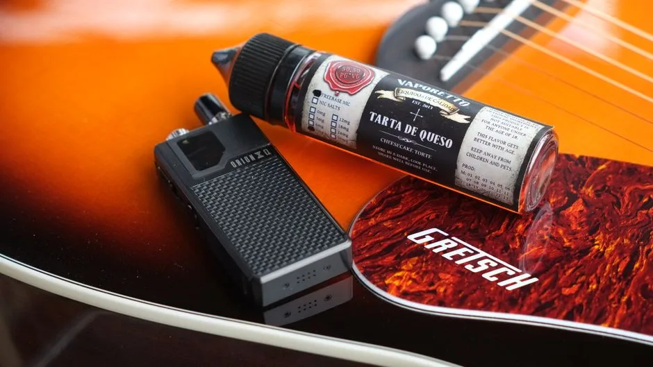 Close-up of an electronic cigarette and liquid bottle on an orange acoustic guitar.