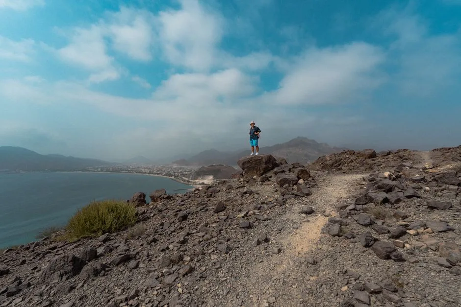 A lone hiker stands atop rocky terrain overlooking Khor Fakkan's coastal beauty in the UAE.